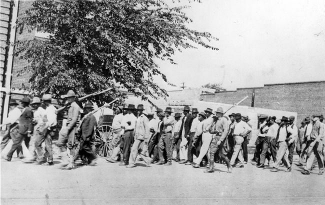 مجموعة من قوات الحرس الوطني ، تحمل بنادق مع حراب مرفقة بها ، ترافق الرجال السود العزل إلى مركز احتجاز بعد مذبحة تولسا ريس ، تولسا ، أوكلاهوما ، يونيو 1921.