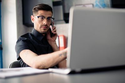 رجل يرتدي نظارات على الهاتف باستخدام الكمبيوتر المحمول
