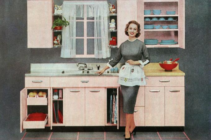 صورة عتيقة لربة منزل عصرية تقف أمام مطبخها الوردي الجديد ، 1957