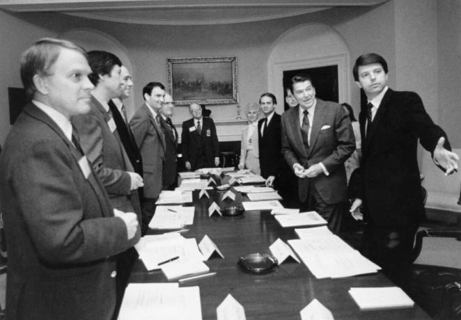 صورة بالأبيض والأسود لرونالد ريغان وعدة رجال آخرين يرتدون بذلات حول طاولة اجتماعات طويلة