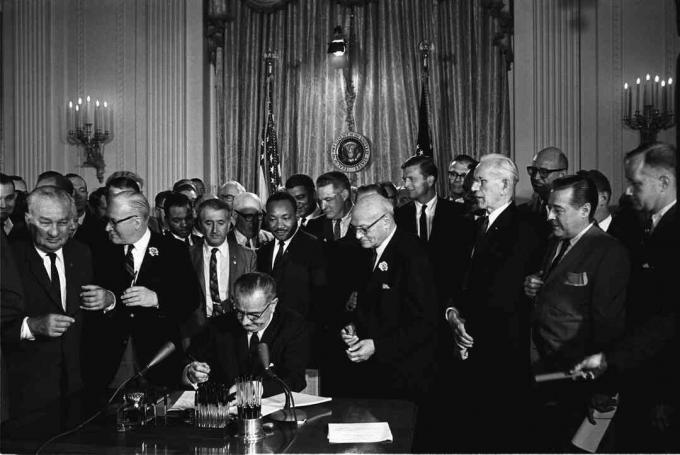 الرئيس ليندون ب. يوقع جونسون على قانون الحقوق المدنية لعام 1964 بينما ينظر إليه مارتن لوثر كينج الابن وآخرون.
